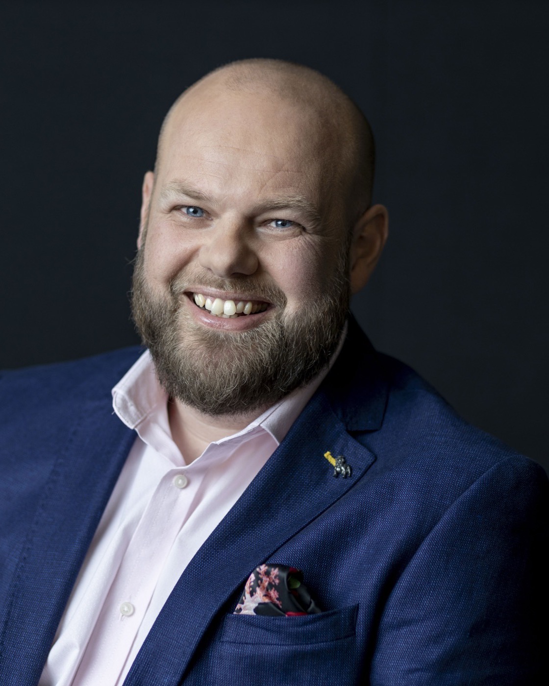 Ben Westlake, smiling, in a navy jacket against a dark studio background